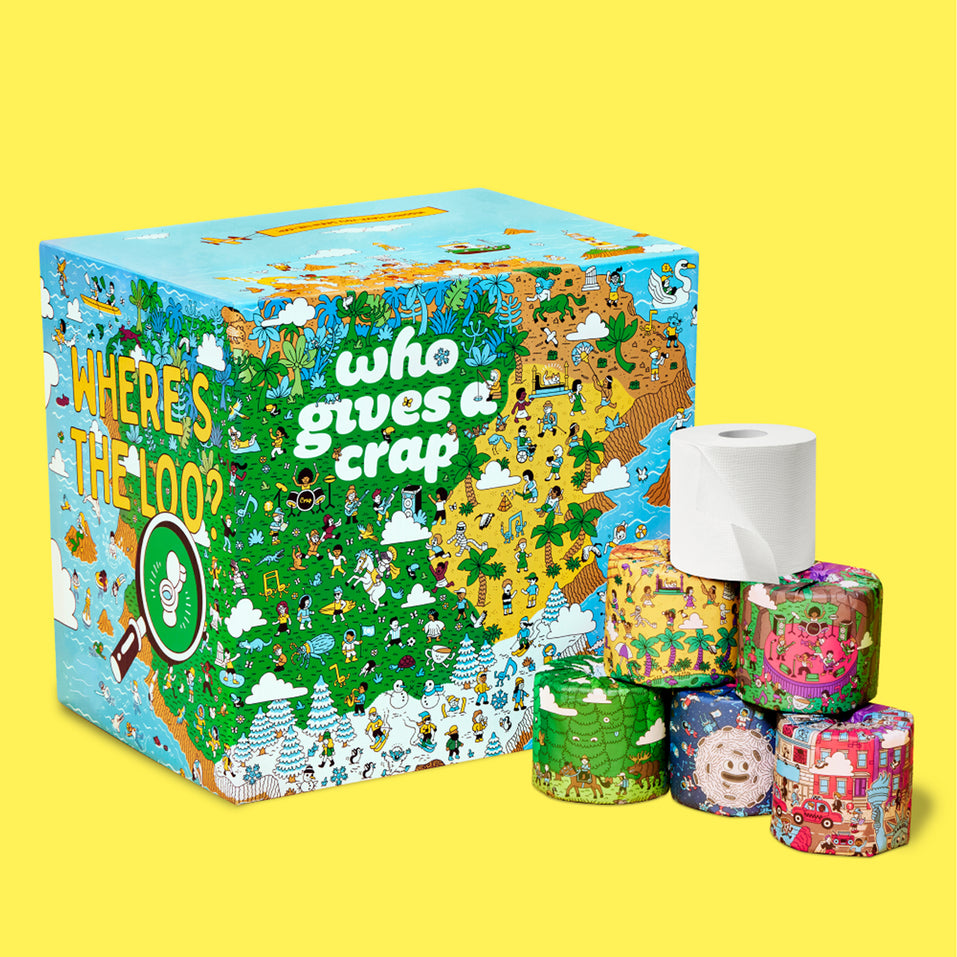 A box of Who Gives A Crap Where’s the Loo Limited Edition toilet paper alongside 6 stacked rolls showcasing different designs.