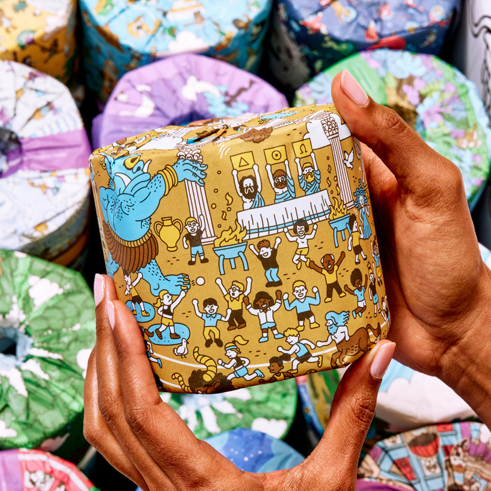 Hands holding a roll of patterned toilet against a background of similar toilet paper rolls.