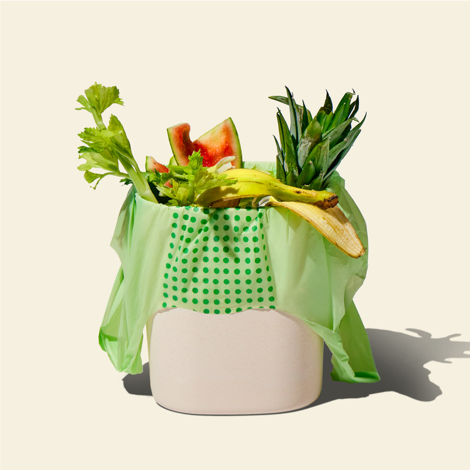 Who Gives a Crap compostable rubbish bag sits in compost bin with food scraps spilling out the top