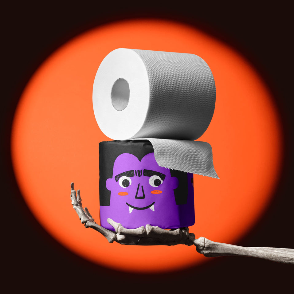 Skeleton hand holding a purple vampire roll of Spooky Edition bamboo toilet paper, unravelling in an orange spotlight